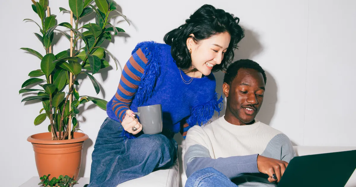 Two people looking at a laptop together next to a houseplant