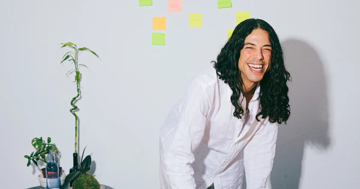A smiling freelancer at a bright desk with plants and sticky notes