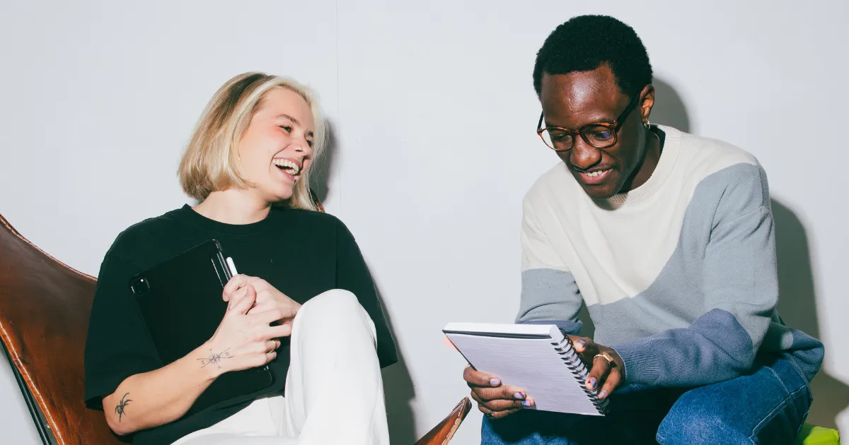 Two people smiling in conversation, one holding a notebook