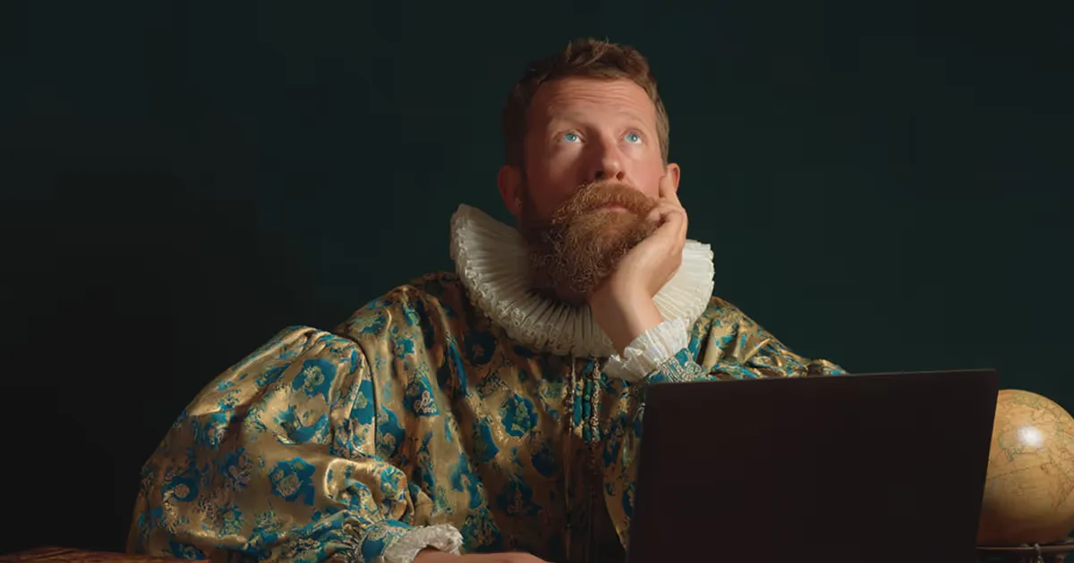 A bearded man looking thoughtfully at a laptop in dim lighting