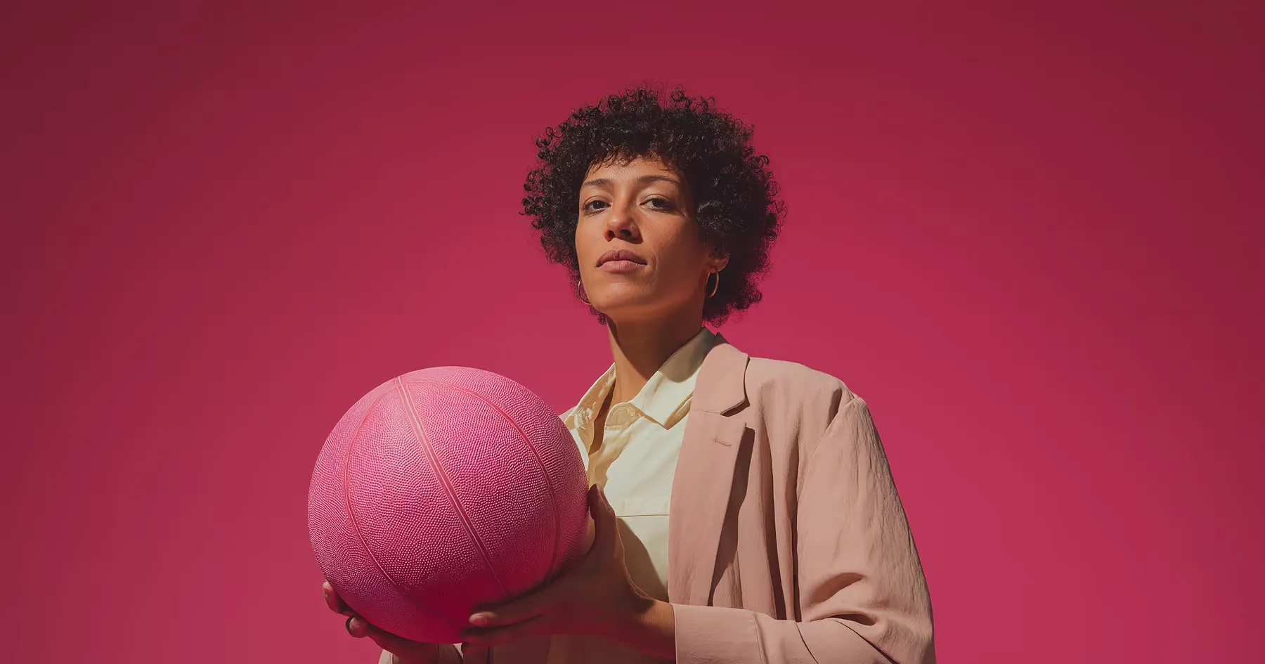A person in a suit holding a pink basketball against a pink background