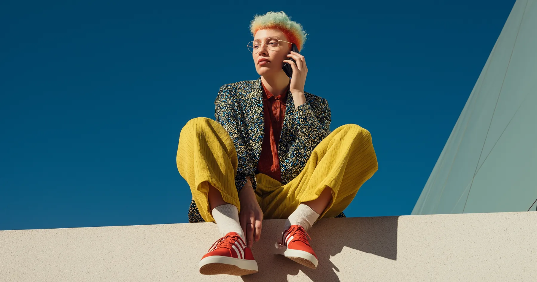 A stylishly dressed person sitting on a ledge talking on the phone