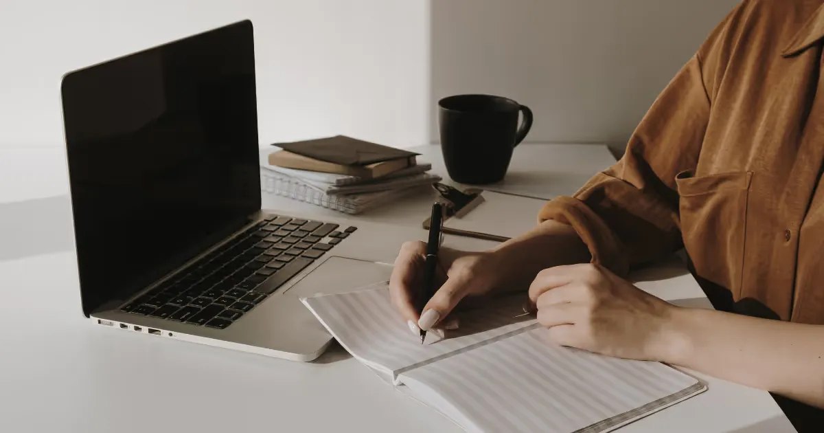 A freelance virtual assistant working remotely at a minimalist desk setup with a laptop, notebook, and coffee cup, symbolizing productivity and professionalism.