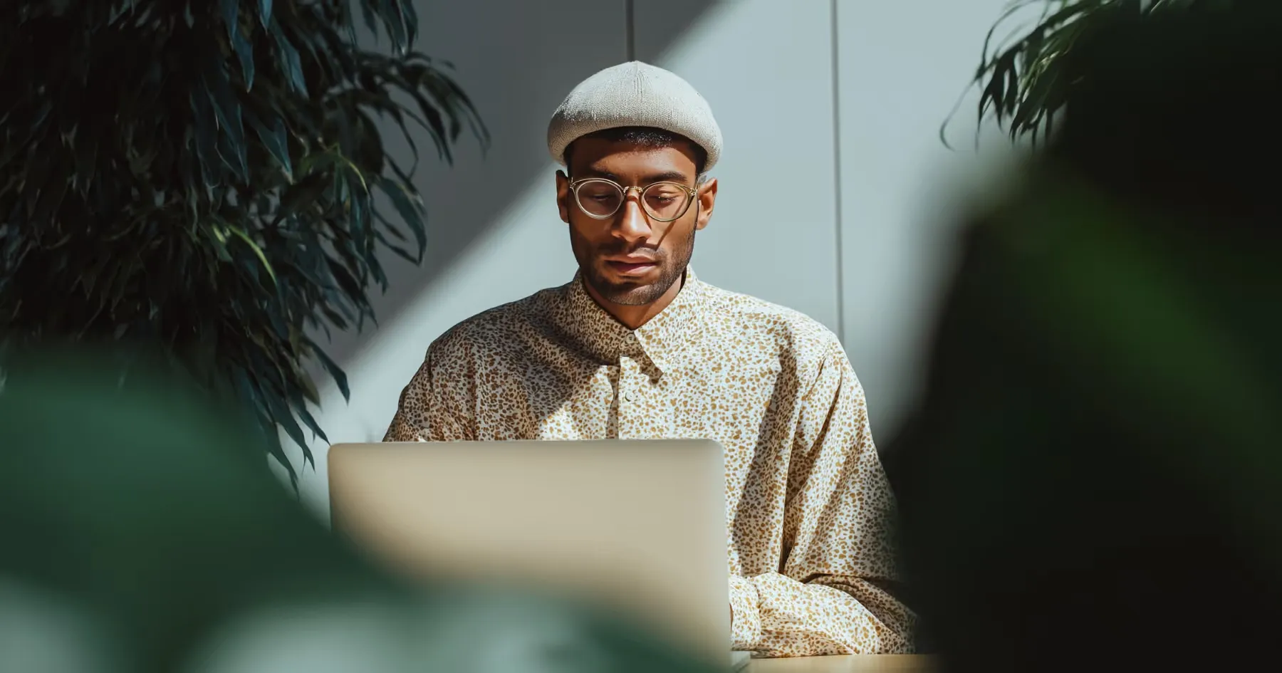 A man in a flat cap working on a laptop in warm light