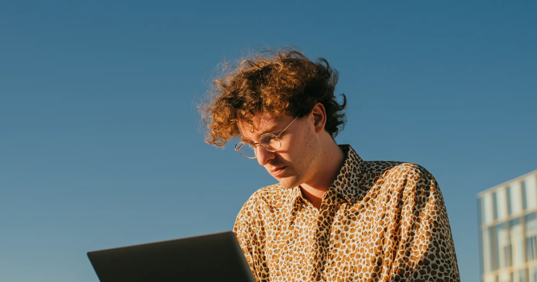 A person with curly hair working on a laptop in sunlight