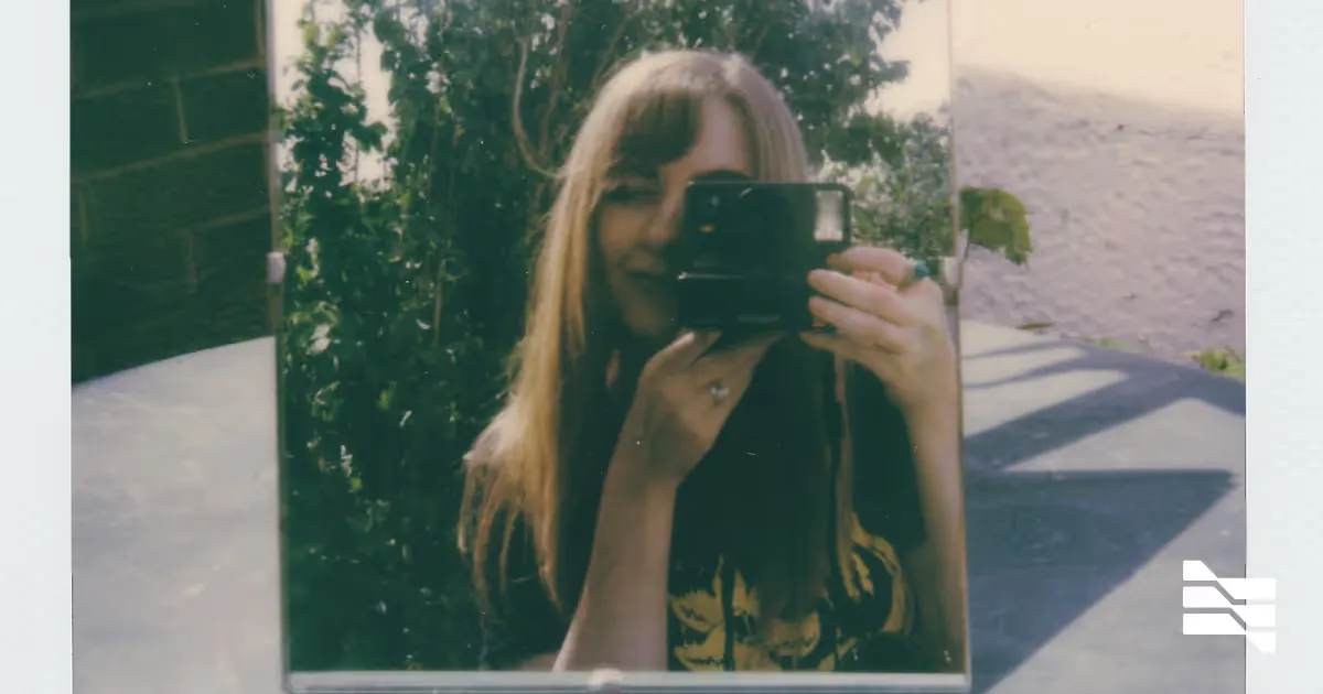 A photographer taking a mirror selfie while holding a camera outdoors