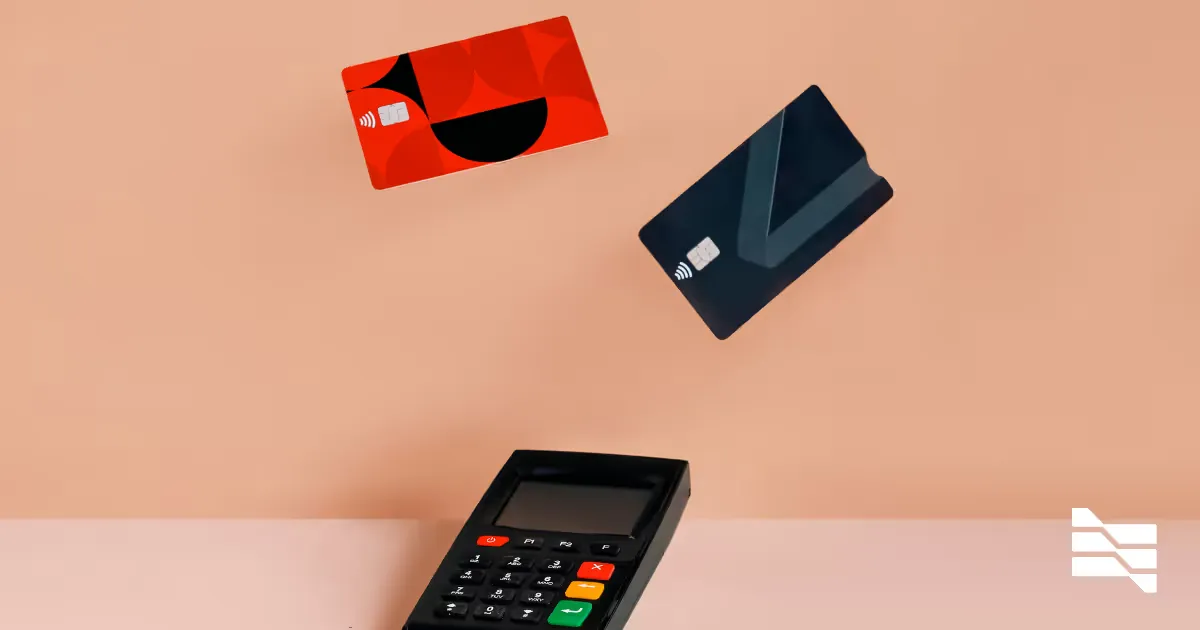 A card payment terminal beside two bank cards on a pink surface